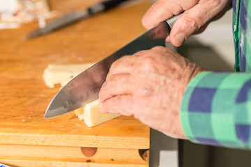 Escena de comida donde destacan salchichones en barra y queso, junto con un cuchillo, listos para cortar o siendo cortados en rodajas o tacos. En una cocina doméstica, en Madrid, España
