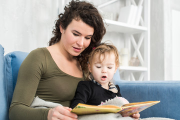 Young mother is reading a book to her cute daughter.