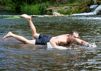 Warm summer day, rest on the nature. A young man is swimming on a very shallow river, he is funny and cheerful.