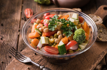 Vegetable salad in glass bowl with broccoli and tomatoes on dark wooden table.