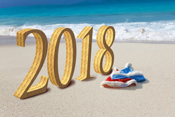 Happy new year card. Two New Year's caps of Santa Claus on beach and inscription 2018 in the sand