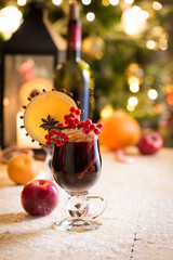 Two high glasses of christmas mulled wine with red apples, orange slices, cinnamon sticks and spices on wooden table with bokeh background. Selective focus.