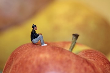 uomo in miniatura seduto su una mela rossa