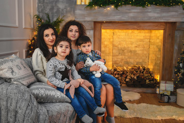 Christmas family portrait of happy smiling mothers hugging their children near to fireplace decorated with fir and garland at home. Winter holiday Xmas and New Year concept