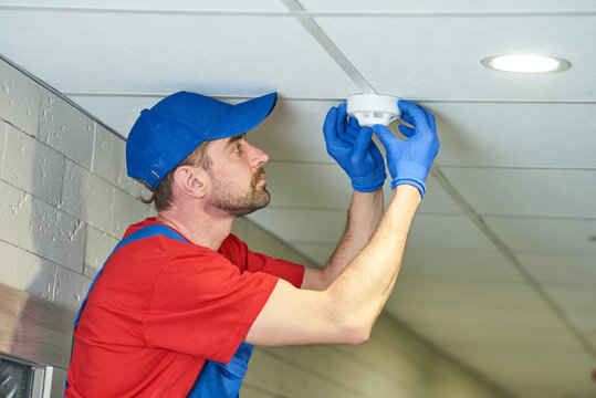 worker installing smoke detector on the ceiling