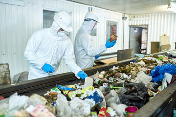 Portrait of two workers  wearing biohazard suits working at waste processing plant sorting trash on conveyor belt, copy space