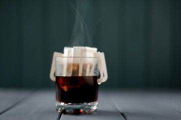 Steaming hot drip coffee in glass on grey background