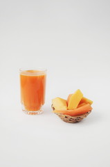 A glass of pumpkin and carrot juice with vegetables on white background. Pieces of pumpkin and carrot on straw plate. Vitamins