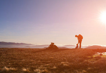 A hiker and their dog on a summit at sunrise on a winters morning in the Derwent Fells, English Lake Distrct, UK.