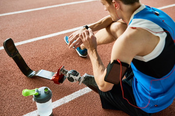 High angle portrait of young amputee athlete sitting on running track taking break from practice and listening to music