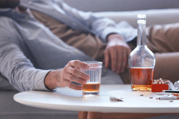 Drunk man lying on sofa with glass of whiskey in hand. Alcoholism concept