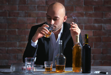 Man drinking whiskey and smoking cigarette at table. Alcoholism concept
