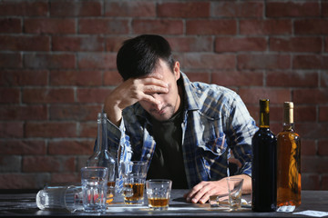 Drunk man sitting at table with alcohol and drugs. Alcoholism concept