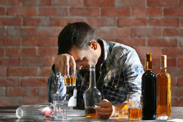 Drunk man sitting at table with alcohol and drugs. Alcoholism concept