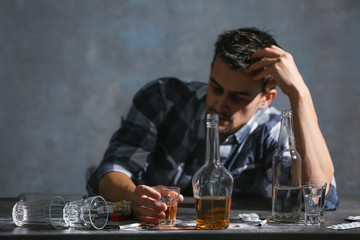 Drunk man sitting at table with alcohol and drugs. Alcoholism concept