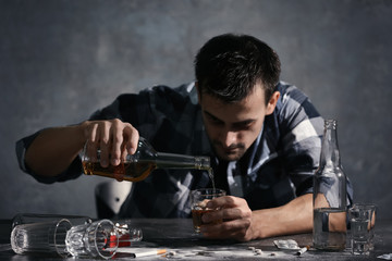 Man sitting at table and pouring whiskey into glass. Alcoholism concept