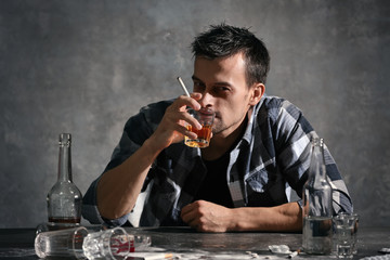 Man drinking alcohol and smoking cigarette while sitting at table
