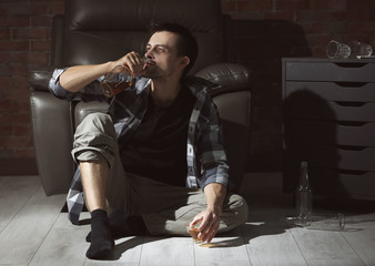 Man sitting on floor at home and drinking whiskey. Alcoholism concept