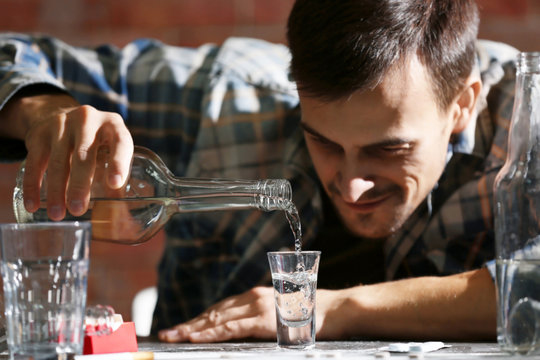 Man sitting at table and pouring alcohol into glass. Alcoholism concept