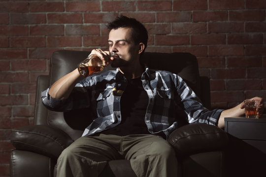 Man sitting in armchair and drinking whiskey. Alcoholism concept