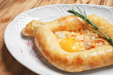 Plate with tasty Adzharian khachapuri on wooden table, closeup