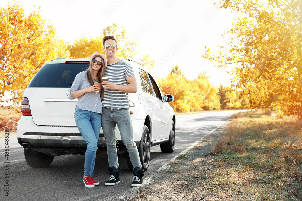 Poster beautiful young couple with coffee standing near car outdoors