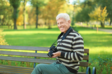 Stylish mature man with camera sitting on bench in autumn park