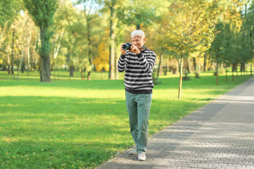 Stylish mature man taking photo in autumn park