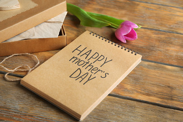 Notebook with words "Happy Mother's day" and pink tulip on wooden background