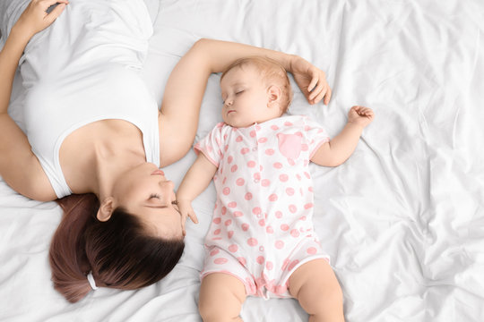 Young mother and cute baby sleeping on bed