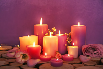 Obraz na płótnie Canvas Purple burning candles with flowers on color background
