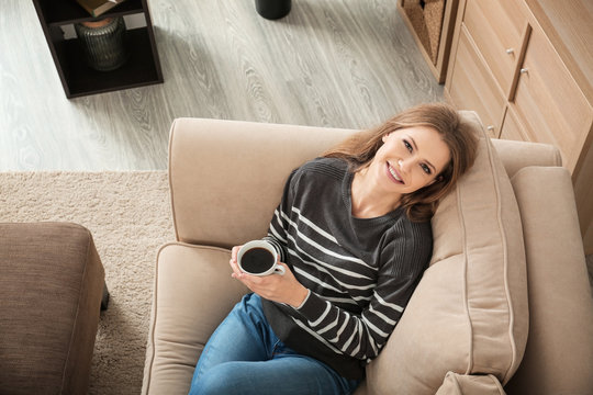 Beautiful woman drinking coffee while resting on sofa at home