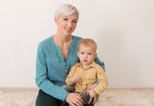 Young mother with her baby sitting on carpet indoors