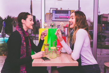Two smiling girls eating cakes and talking in cafe