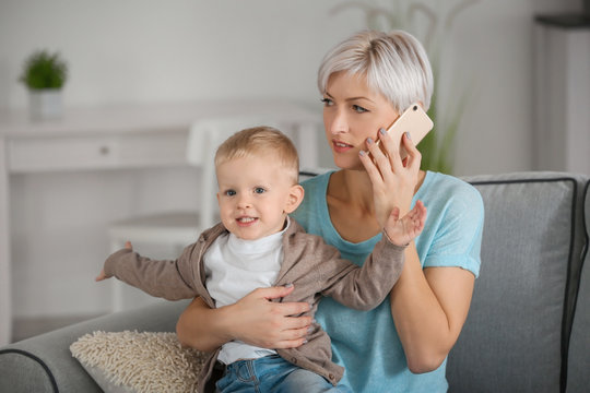 Young mother talking on phone while holding her baby at home