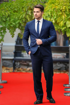 Handsome young man in black suit on red carpet, outdoors