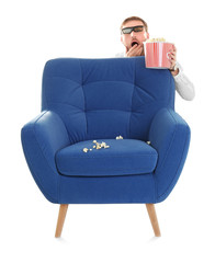 Naklejka premium Scared man with 3d glasses and popcorn hiding behind armchair during cinema show on white background