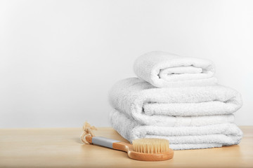 Clean towels and bath brush on table against light background