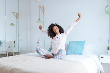 Happy beautiful young black woman relaxed sitting in the bed .