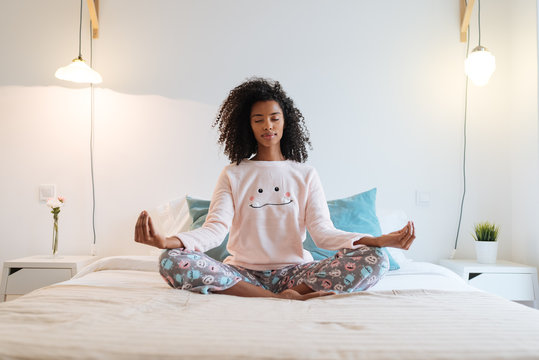 Happy Beautiful Young Black Woman Relaxed  At Home Doing Morning Meditation In Bed .