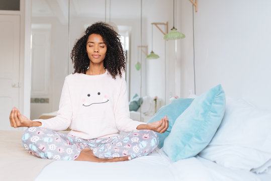 Happy beautiful young black woman relaxed  at home doing morning meditation in bed .