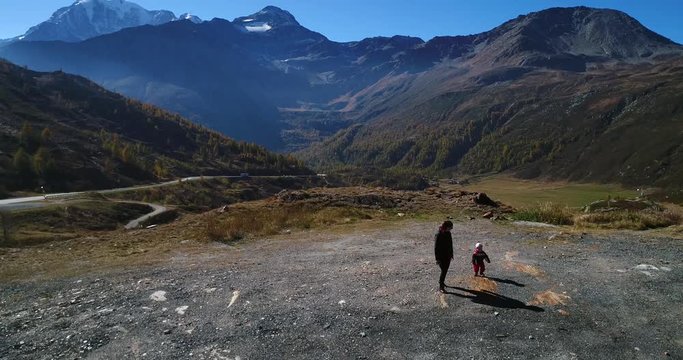 Woman and child, Cinema 4k aerial backward view of a mother and a kid, walking from a mountain ledge towards a car, on a sunny fall day, on simplon pass, in wallis, of the alps in Switzerland