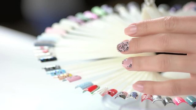 Hand and nail design samples. Woman in nail salon choosing design. Selection of color shellac nail polish.