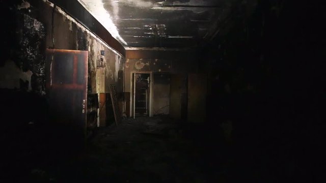 The interior or dark corridor of the burnt down building after the fire, is illuminated at night by a lantern, burnt furniture, walls in soot