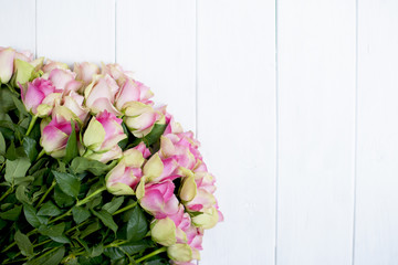 big bouquet of roses with pink petals and green on white wooden background