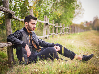 Fototapeta premium Portrait of sexy young man looking to a side while leaning on wooden fence in countryside