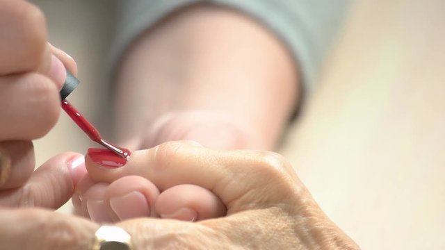 Manicurist applying red varnish to senior woman. Nail beautician painting nails to old woman in beauty salon close up.