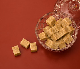 Cane sugar cubes in the sugar bowl on red background