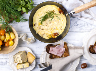 omelette with tomato for breakfast, cheese and greens on white wooden background