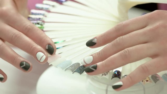 Female hands and wheel of nail art. Young woman hands with modern manicure design and nail art samples in beauty salon.
